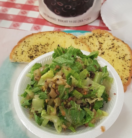 A fresh salad with greens and toppings, served with two slices of garlic bread on a checkered tablecloth.