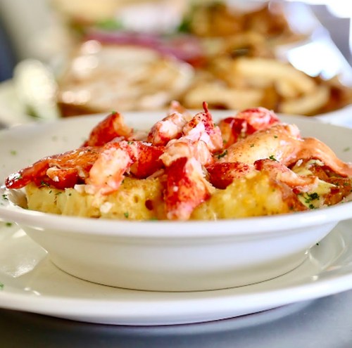 A bowl of creamy lobster mac and cheese topped with chunks of lobster and garnished with parsley.