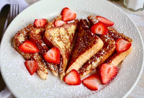 A plate of French toast slices topped with fresh strawberries and powdered sugar.