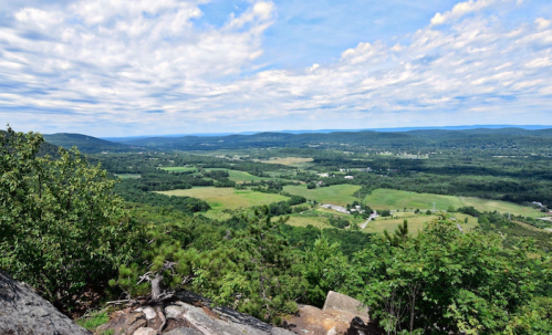 A panoramic view of lush green valleys and rolling hills under a partly cloudy sky.