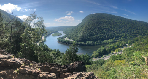 A panoramic view of a river winding through lush green hills under a clear blue sky.