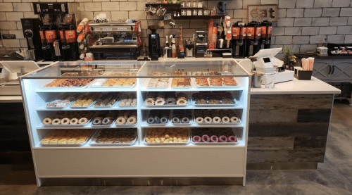 A display case filled with various donuts and pastries in a modern café setting.