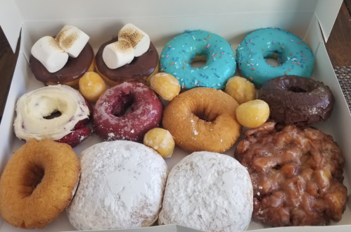 A box of assorted donuts, including chocolate, glazed, and colorful varieties, with some topped with sprinkles and marshmallows.