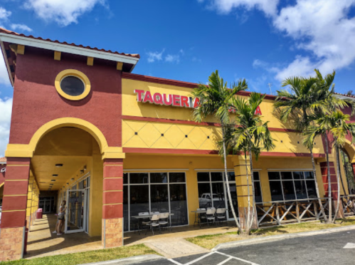 Colorful exterior of a taqueria with palm trees and blue skies in the background.