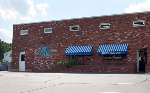 Exterior of Tony's Seafood, a brick building with blue and white striped awnings and an "Open" sign in the window.