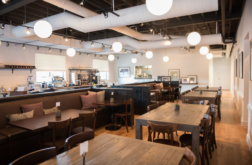 A modern restaurant interior with wooden tables, cozy seating, and round pendant lights hanging from the ceiling.