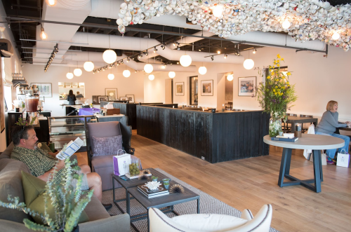 A modern, airy interior of a café with seating areas, artwork on the walls, and decorative lighting.