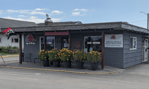 A small restaurant with a gray exterior, flower pots, and a sign displaying a reader's choice award.