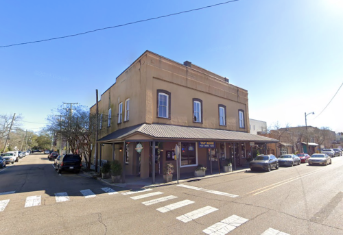 A corner building with a restaurant on the ground floor, surrounded by parked cars and clear blue skies.