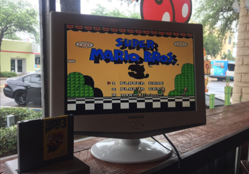 A monitor displaying the title screen of "Super Mario Bros. 3" with a game cartridge beside it.