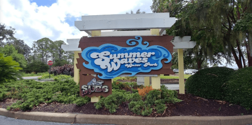 Colorful sign for Summer Waves Water Park, featuring blue waves and tropical greenery in the background.