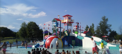 A colorful water park with slides and a play structure, filled with people enjoying the sunny day.