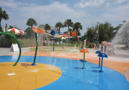 A colorful splash pad with water features and children playing under sprays of water on a sunny day.
