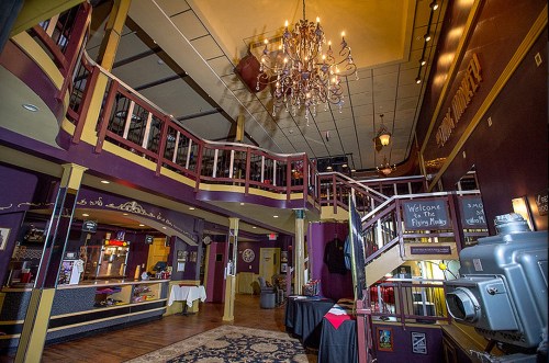Interior of a vintage theater with a chandelier, balcony, and colorful decor, featuring a welcoming atmosphere.