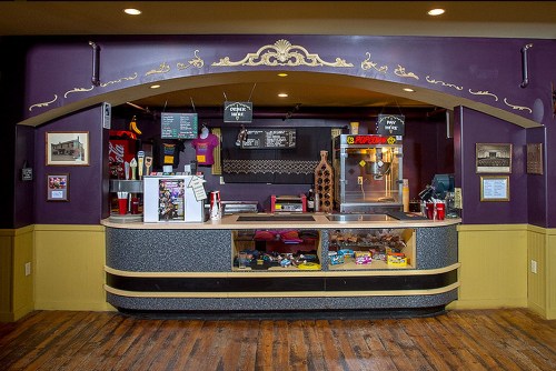 A vintage-style concession stand with snacks, drinks, and a popcorn machine, set against a purple wall.