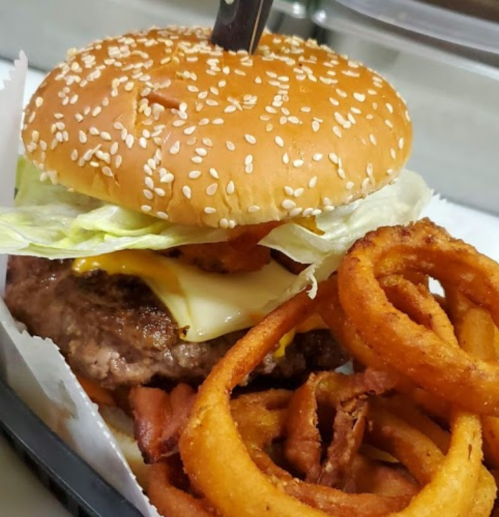 A juicy cheeseburger with lettuce and a sesame seed bun, served with crispy onion rings on the side.