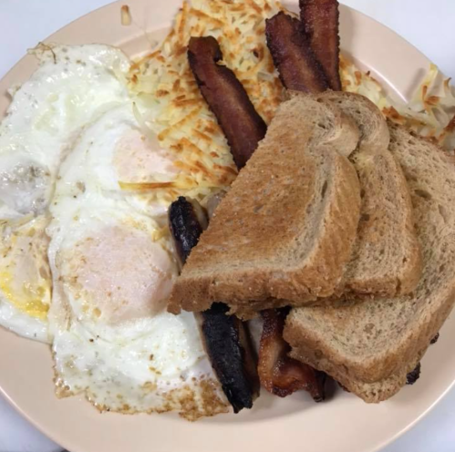 A plate with two fried eggs, hash browns, crispy bacon, and slices of toasted bread.