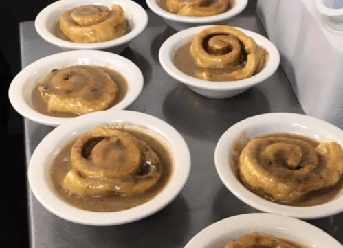 Cinnamon rolls in small white bowls, topped with a glossy caramel sauce.