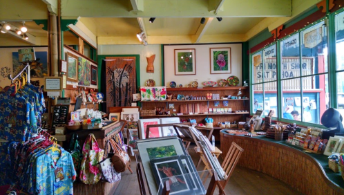 A vibrant art shop filled with colorful artwork, crafts, and clothing, featuring wooden shelves and a cozy atmosphere.