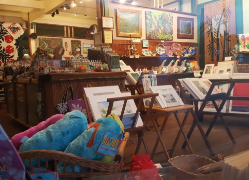 A colorful art shop interior with paintings, crafts, and plush toys displayed on tables and shelves.