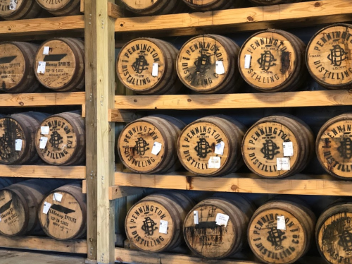 A wooden rack filled with barrels labeled "Pennington Distilling," showcasing a rustic distillery interior.