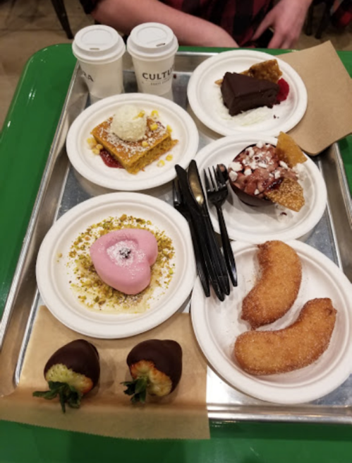 A tray with various desserts: chocolate cake, pastries, a pink heart-shaped treat, and chocolate-covered strawberries.