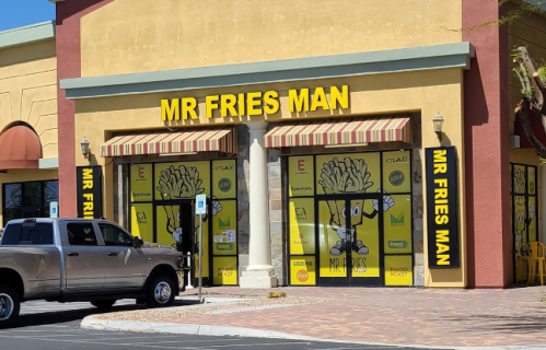 Exterior of "Mr Fries Man" restaurant with bright yellow signage and a parked truck in front. Clear blue sky above.
