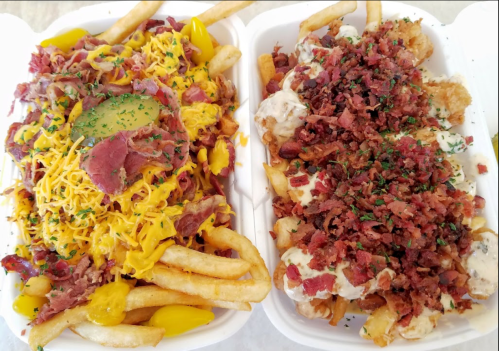 Two trays of loaded fries: one topped with cheese, bacon, pickles, and jalapeños; the other with bacon and creamy sauce.