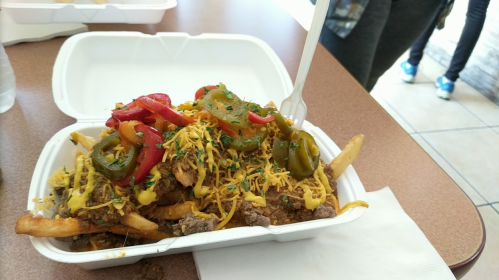 A takeout container filled with loaded fries topped with cheese, jalapeños, and colorful bell peppers.