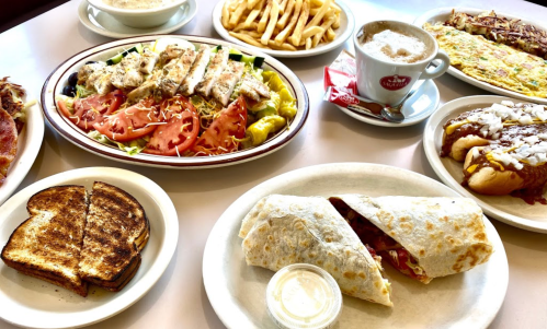 A spread of various dishes including a salad, fries, a wrap, toast, and a hot dog, with a coffee on the side.