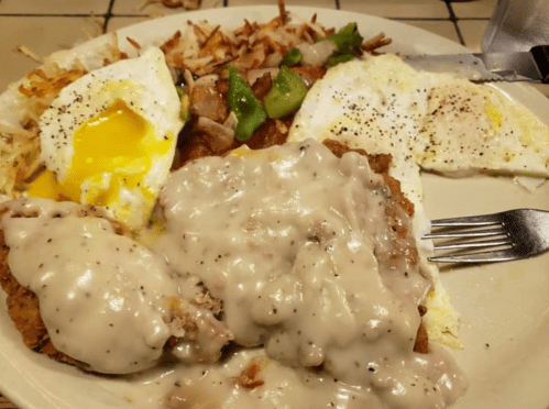A plate of breakfast featuring eggs, hash browns, green peppers, and chicken fried steak topped with gravy.