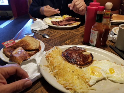 A breakfast spread featuring eggs, hash browns, bacon, toast, and condiments on a wooden table.