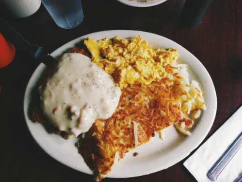 A plate of breakfast featuring scrambled eggs, hash browns, and a biscuit topped with creamy gravy.