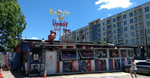 A colorful bar with a quirky sign reading "I'm Dyin' for Daddy" and a large pink pig figure on the roof.