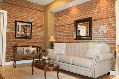 Cozy living room with exposed brick walls, a beige sofa, decorative pillows, a wooden coffee table, and framed artwork.