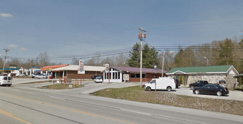 A roadside view of several businesses, including a restaurant and a stone building, with cars parked outside.