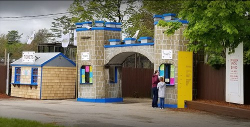 A ticket booth resembling a castle entrance, with two people at the window and colorful signs displayed.