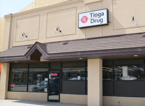 Exterior of Tioga Drug store with a sign and open door, featuring a simple architectural design.