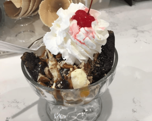 A dessert bowl with brownie pieces, vanilla ice cream, nuts, chocolate sauce, whipped cream, and a cherry on top.