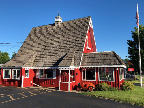 A charming red building with a steep roof, featuring white trim and a small garden, set against a clear blue sky.