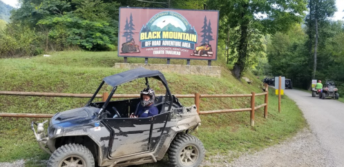 A person in an ATV near a sign for Black Mountain Off Road Adventure Area in Kentucky, surrounded by trees.