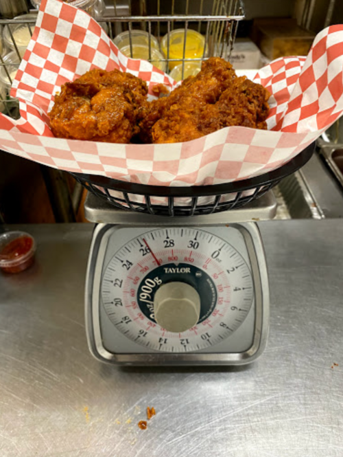 A basket of fried chicken wings on a scale, showing a weight of 190 grams, with condiments in the background.