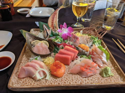 A beautifully arranged sashimi platter with various fish, garnished with flowers and served with wasabi and sauces.