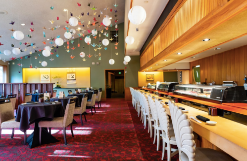 Interior of a restaurant featuring elegant decor, hanging paper cranes, and a sushi bar with seating arrangements.