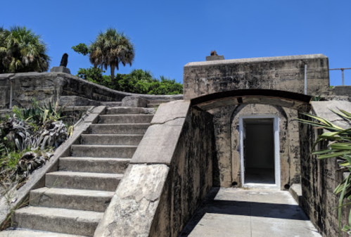Weathered stone steps lead to an archway entrance, surrounded by lush greenery and a clear blue sky.