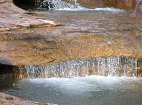 A serene waterfall cascading over smooth rocks into a clear pool of water.
