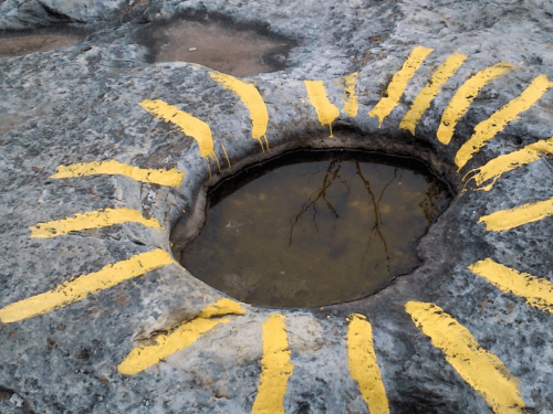 A circular stone basin with yellow rays painted around it, reflecting a tree in the water.