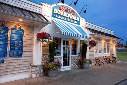 Exterior of Iggy’s Boardwalk, a lobster and clam bar, featuring a striped awning and flower baskets at dusk.