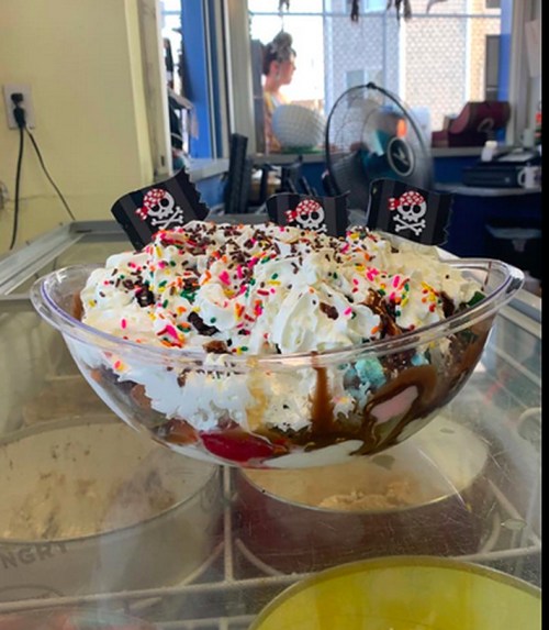 A large ice cream sundae topped with whipped cream, sprinkles, and chocolate sauce, served in a glass bowl.