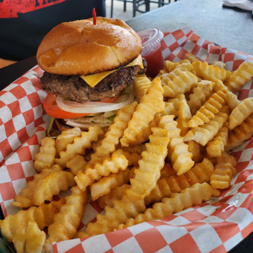 A juicy cheeseburger with lettuce, tomato, and a side of crinkle-cut fries in a red-checkered basket.